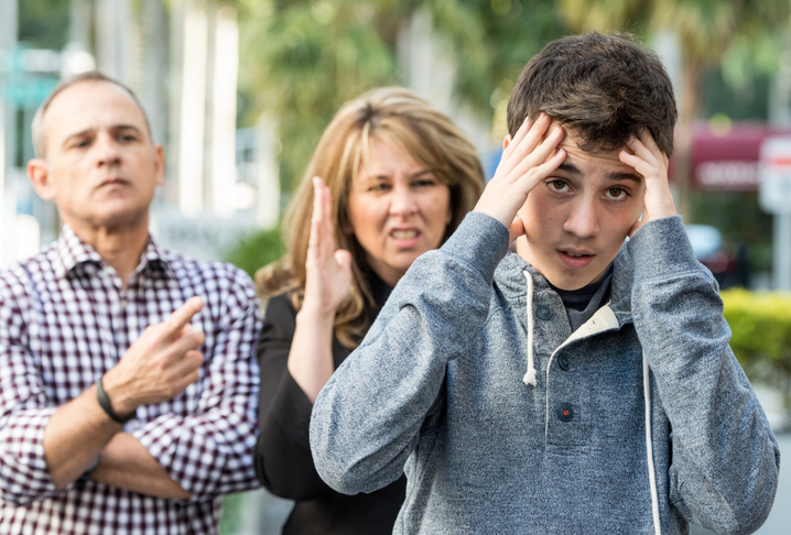 Serious Teenage boy posing with his very upset parents in the background
